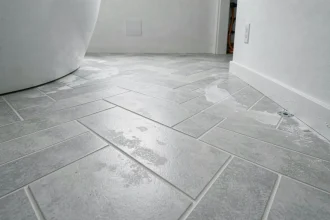 Carrelage en chevron gris posé sur plancher chauffant dans une salle de bain moderne, avec joints fins et détails de pose soignés