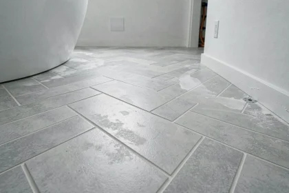 Carrelage en chevron gris posé sur plancher chauffant dans une salle de bain moderne, avec joints fins et détails de pose soignés