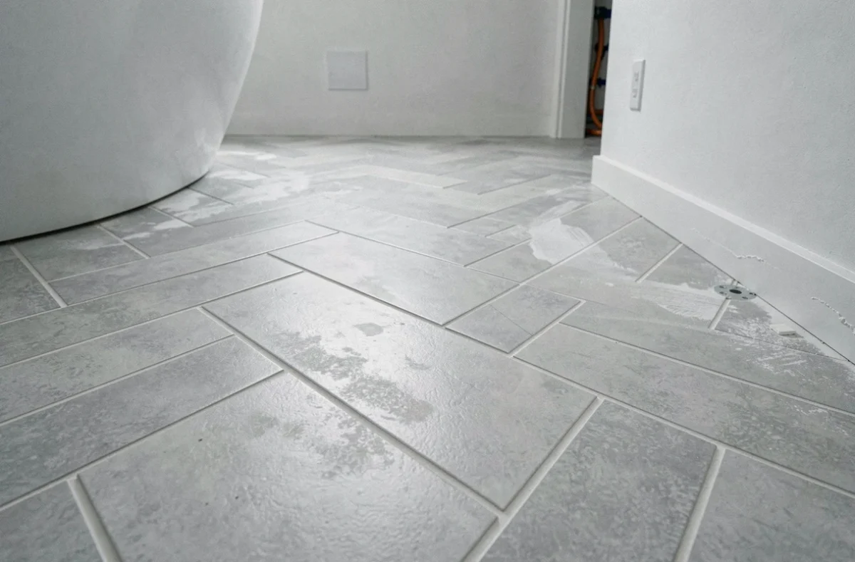 Carrelage en chevron gris posé sur plancher chauffant dans une salle de bain moderne, avec joints fins et détails de pose soignés